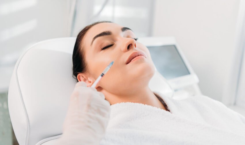 cropped shot of cosmetologist in latex glove with syringe making beauty injection to beautiful woman
