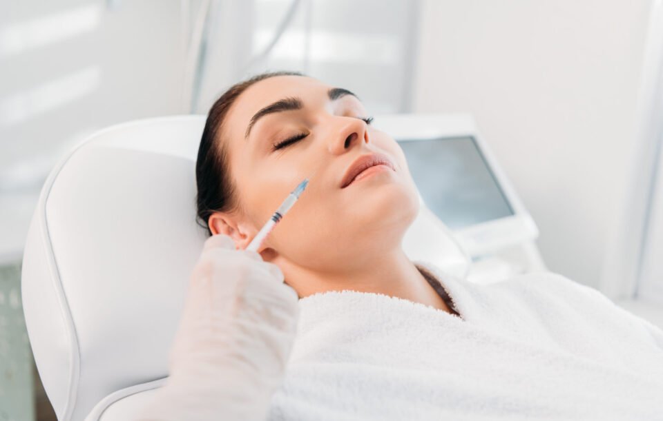 cropped shot of cosmetologist in latex glove with syringe making beauty injection to beautiful woman